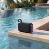 Black portable Bluetooth speaker with LED trim, shown poolside outdoors