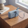 Blue portable wireless speaker charging on wooden bedside table