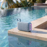 Blue portable Bluetooth speaker with fabric finish beside outdoor swimming pool