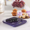 Digital kitchen scale in purple weighing fresh blueberries on kitchen counter