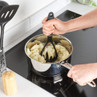 Mashing potatoes in a saucepan with a black plastic potato masher on a kitchen hob