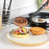Cooked burger patty being placed on bun with salad, onions and pickles, kitchen setting
