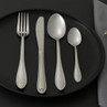 Four-piece silver cutlery set on black plate, including fork, knife, spoon and teaspoon