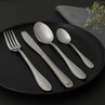 Four-piece stainless steel cutlery set on black plate, includes fork, knife, dessert spoon and teaspoon.