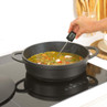 Black casserole dish on induction hob with food, digital thermometer checking temperature