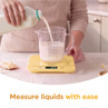 Person pouring milk into a measuring jug on yellow digital kitchen scales