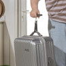 Silver hard shell suitcase held by strap, shown at home doorway