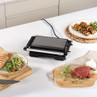 Black electric grill closed on kitchen counter, surrounded by raw steak, salad, and skewers