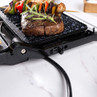 Electric grill with steak and vegetable skewers cooking, shown on a marble worktop