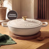 Cream cast iron casserole dish with lid and gold handle, shown on wooden board