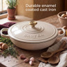 Cream enamel cast iron casserole dish with lid and gold knob on rustic kitchen table