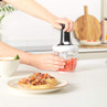Hand using manual food chopper to dice red vegetables in a kitchen setting