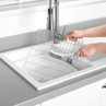 Stainless steel sink grid being cleaned with a dish brush in a white kitchen sink