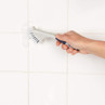 Hand cleaning white tiled grout with angled cleaning brush