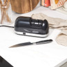 Electric knife sharpener and black-handled kitchen knife on white countertop