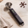 Digital measuring spoon with screen and buttons, shown on a kitchen counter