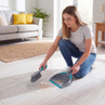 Grey dustpan and brush set in use, sweeping crumbs from light wood floor