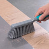Grey sweeping brush with teal handle sweeping dust from wooden and tiled floor