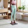 Digital bathroom scale in use on tiled floor, shown with person in pastel workout clothes
