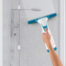 Hand using teal and white electric window vacuum to clean shower screen