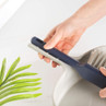 Hand holding a navy and grey dustpan and brush set with bristles, on white surface.