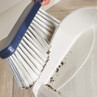 Hand sweeping dust into white dustpan with blue brush