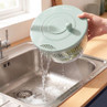 Green salad spinner draining water into sink, held by hand, for kitchen use