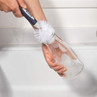 Bottle brush cleaning a clear glass bottle with soap suds at a kitchen sink