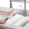 Bottle brush cleaning a clear glass bottle under running tap in kitchen sink