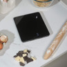 Black digital kitchen scale on worktop with eggs, chocolate and rolling pin