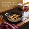 Cream cast iron frying pan with pancakes on hob, highlighting PFAS free coating feature