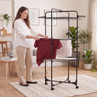 Black folding indoor clothes airer with laundry, shown in modern living room
