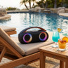 Portable black Bluetooth speaker with colourful lights, shown on poolside lounger