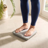 Person standing on silver mechanical bathroom scale, feet visible, in light room