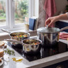 Set of 3 silver saucepans with glass lids on induction hob, cooking vegetables