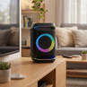 Black portable Bluetooth speaker with multicolour LED lights, shown on a living room table
