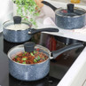 Set of three non-stick speckled saucepans with glass lids on a modern induction hob