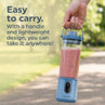 Blue portable blender with handle, filled with pink smoothie, shown outdoors.