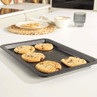 Non-stick baking tray with five chocolate chip cookies, shown on a kitchen worktop.