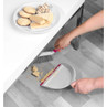 Hand using pink and white dustpan and brush to sweep biscuit crumbs from light wood floor