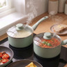 Set of two green saucepans with glass lids, steaming on a hob in a kitchen setting