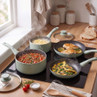 Set of four mint green saucepans and frying pans in use on a hob, shown with cooked food