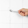 Hand cleaning white tiled grout with scrubbing brush and foam