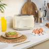 Cream two-slice toaster on kitchen counter, with eggs and avocado toast nearby