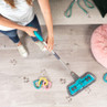 Person mopping muddy paw prints from light wood floor, next to pet toys. Cleaning product in use.