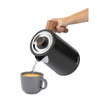 Black electric kettle with wood-effect handle pouring hot water into grey mug