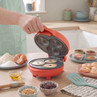 Red mini doughnut maker with three ring doughnuts cooking on kitchen counter