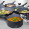 Set of non-stick black saucepans and frying pans with cooked meals, lids included