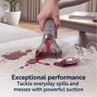 Handheld carpet cleaner removing red wine spill from light fabric sofa