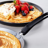 Non-stick pancake pan with freshly cooked pancake, plate of pancakes topped with whipped cream and mixed berries.